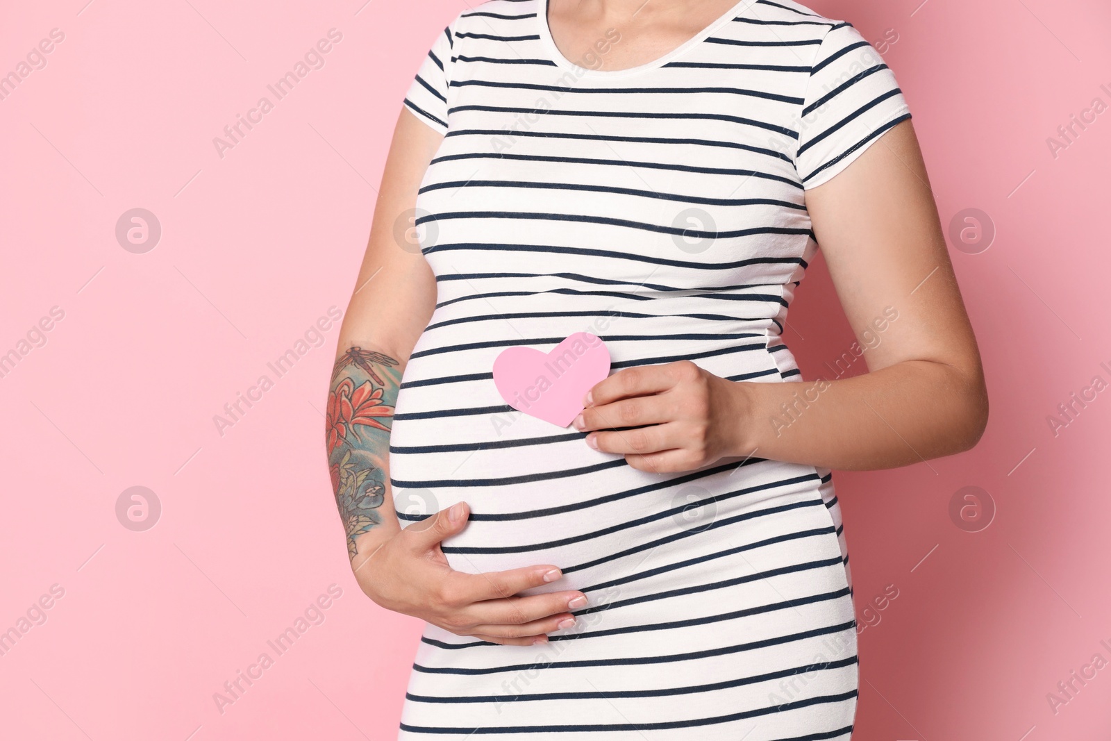 Photo of Pregnant woman with paper heart on pink background, closeup