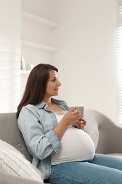 Photo of Beautiful pregnant woman with cup on sofa at home