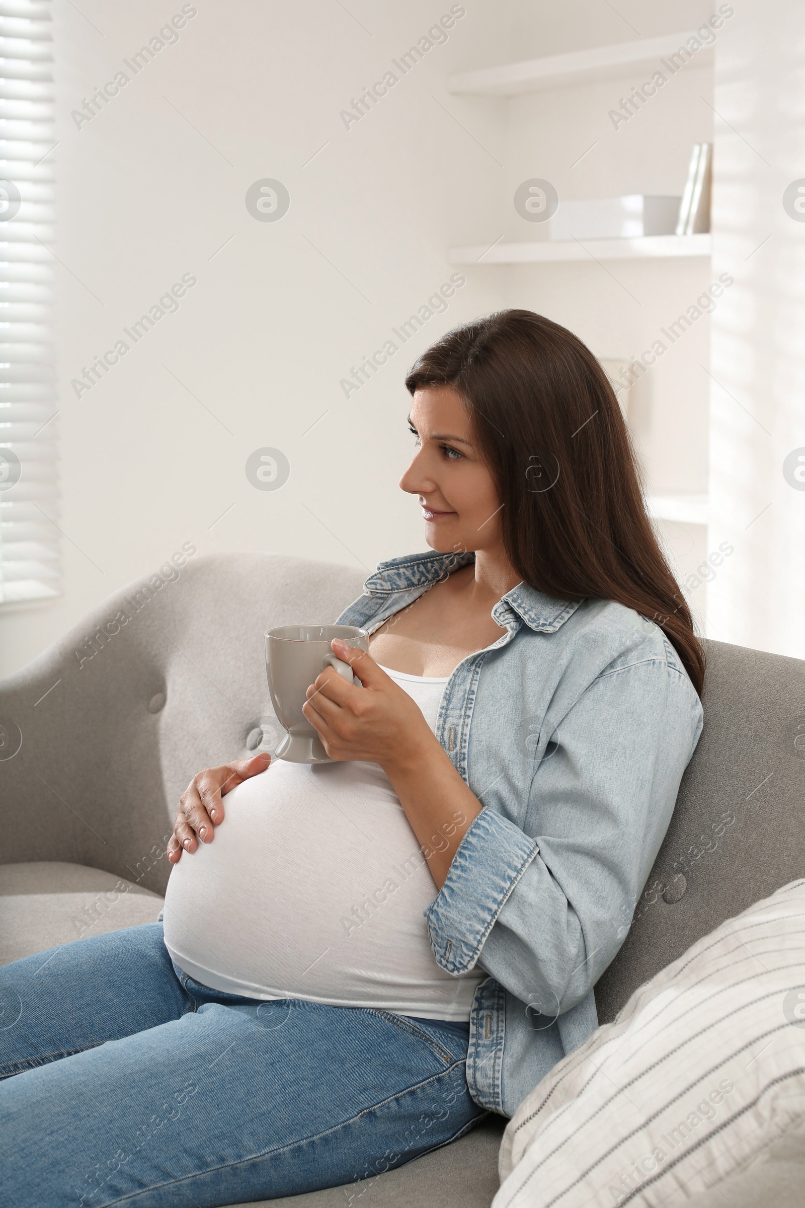 Photo of Beautiful pregnant woman with cup on sofa at home