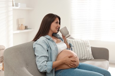 Photo of Beautiful pregnant woman with cup on sofa at home