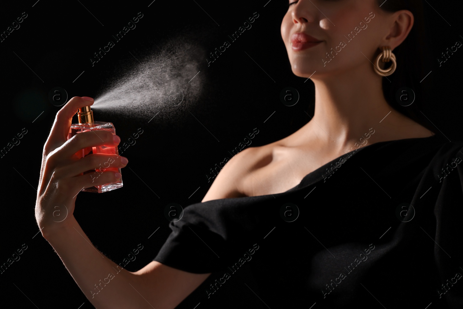 Photo of Woman spraying perfume on black background, closeup