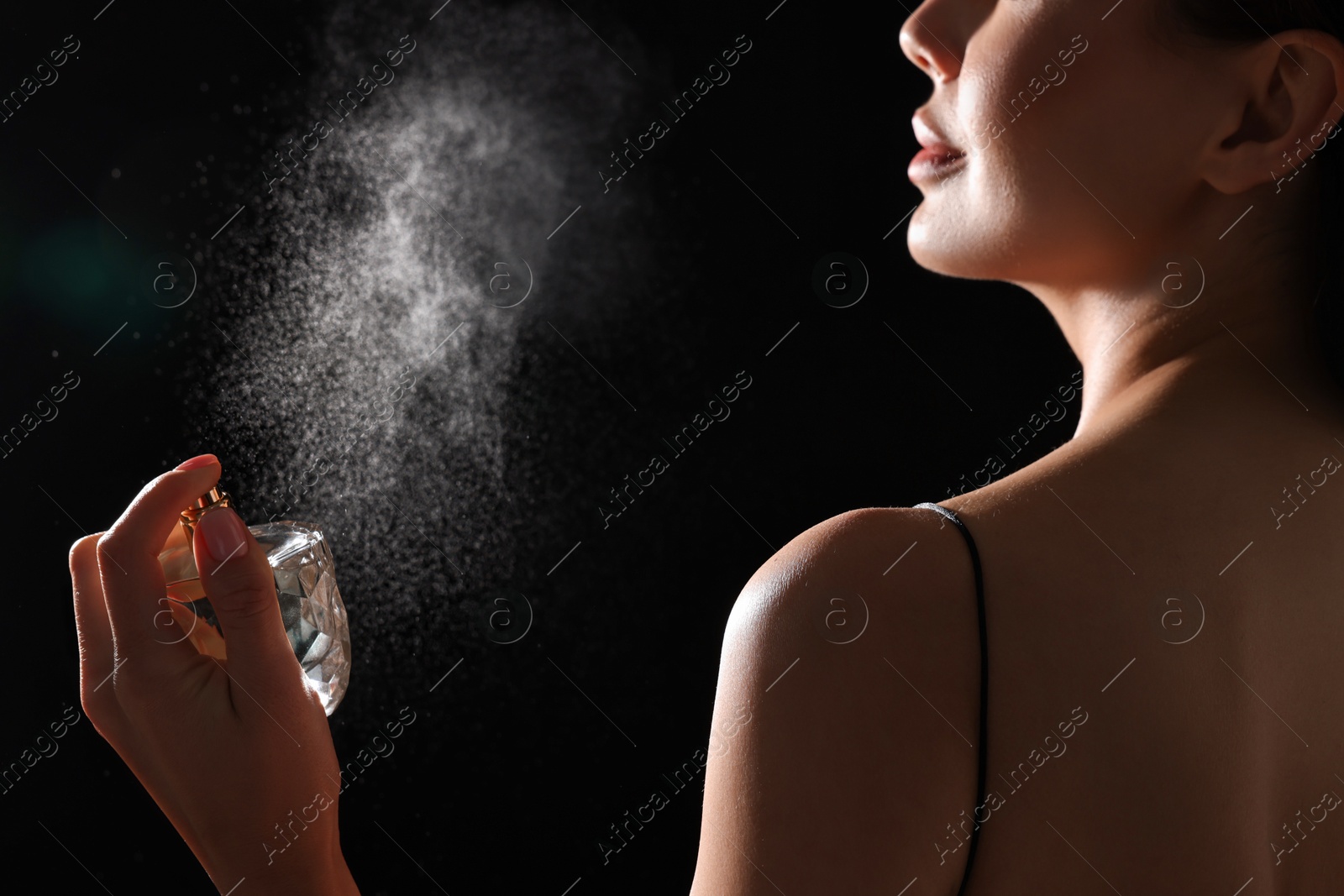 Photo of Woman spraying perfume on black background, back view