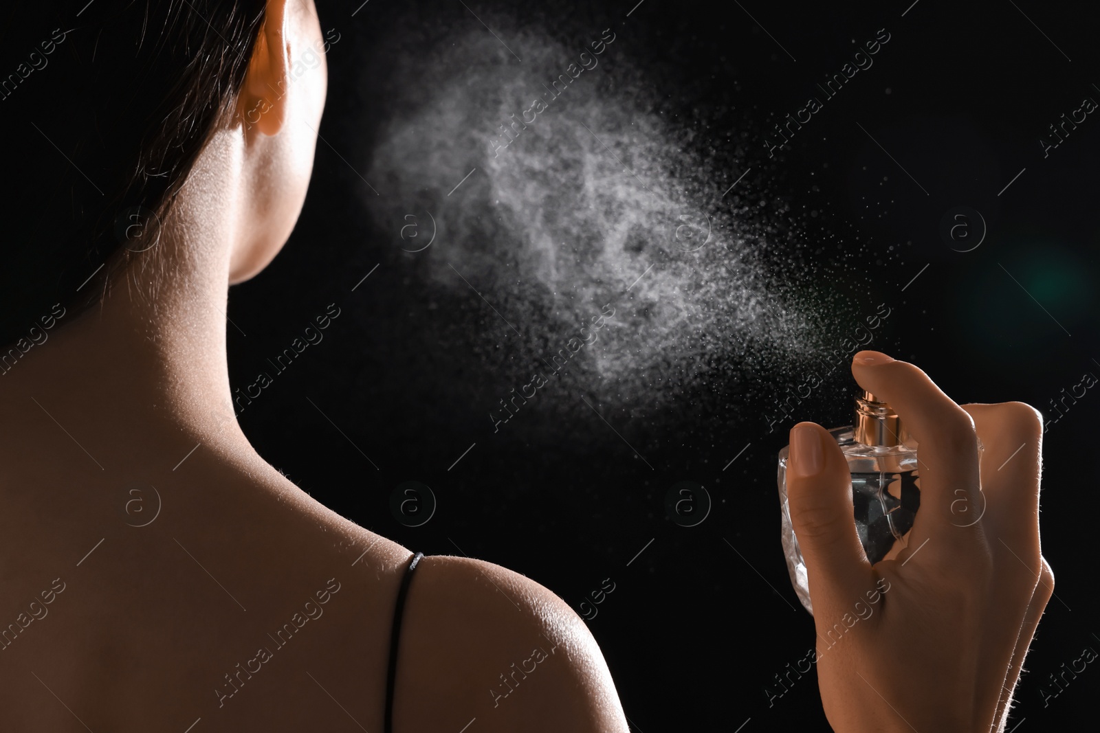 Photo of Woman spraying perfume on black background, back view