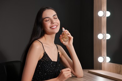 Photo of Smiling woman with bottle of perfume in makeup room