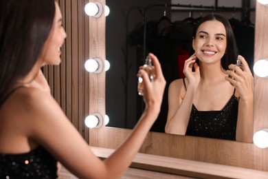 Photo of Smiling woman with bottle of perfume near mirror in makeup room