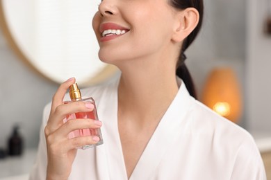 Photo of Smiling woman spraying aromatic perfume indoors, closeup