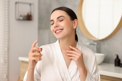 Photo of Smiling woman spraying aromatic perfume in bathroom