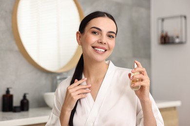 Photo of Smiling woman with bottle of perfume in bathroom