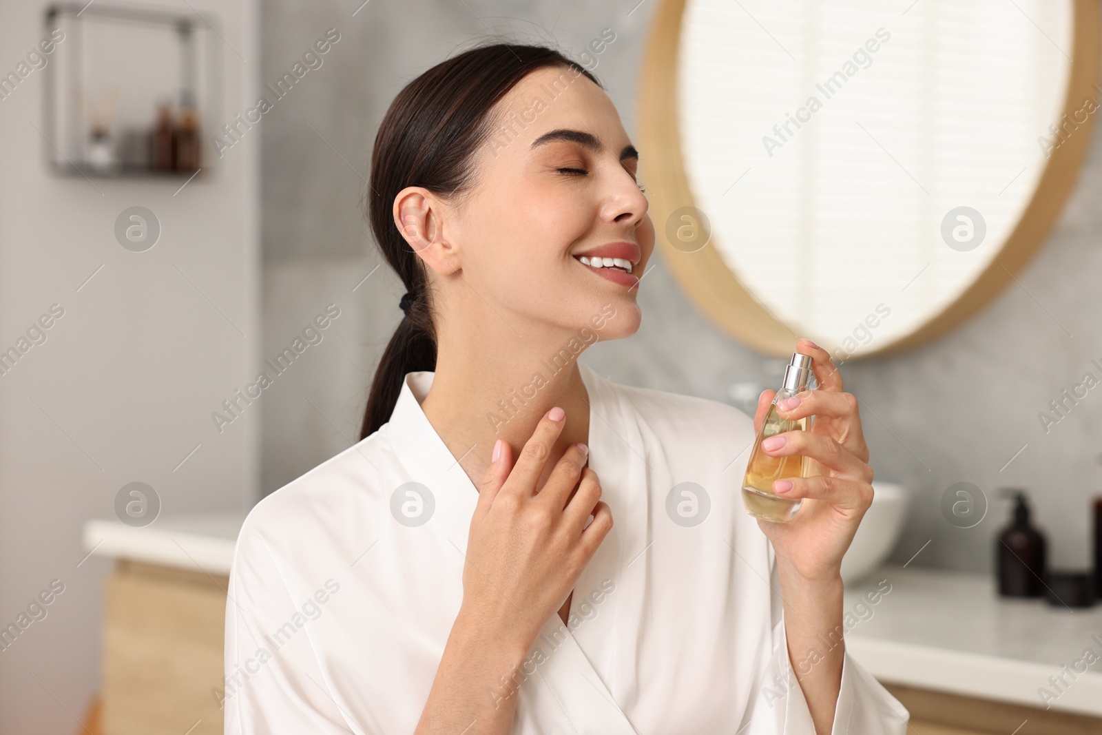 Photo of Smiling woman with bottle of perfume in bathroom