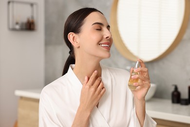 Photo of Smiling woman with bottle of perfume in bathroom