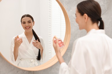 Smiling woman with bottle of perfume near mirror in bathroom