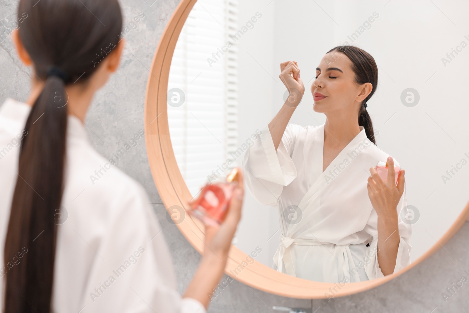 Photo of Beautiful woman smelling perfume near mirror in bathroom