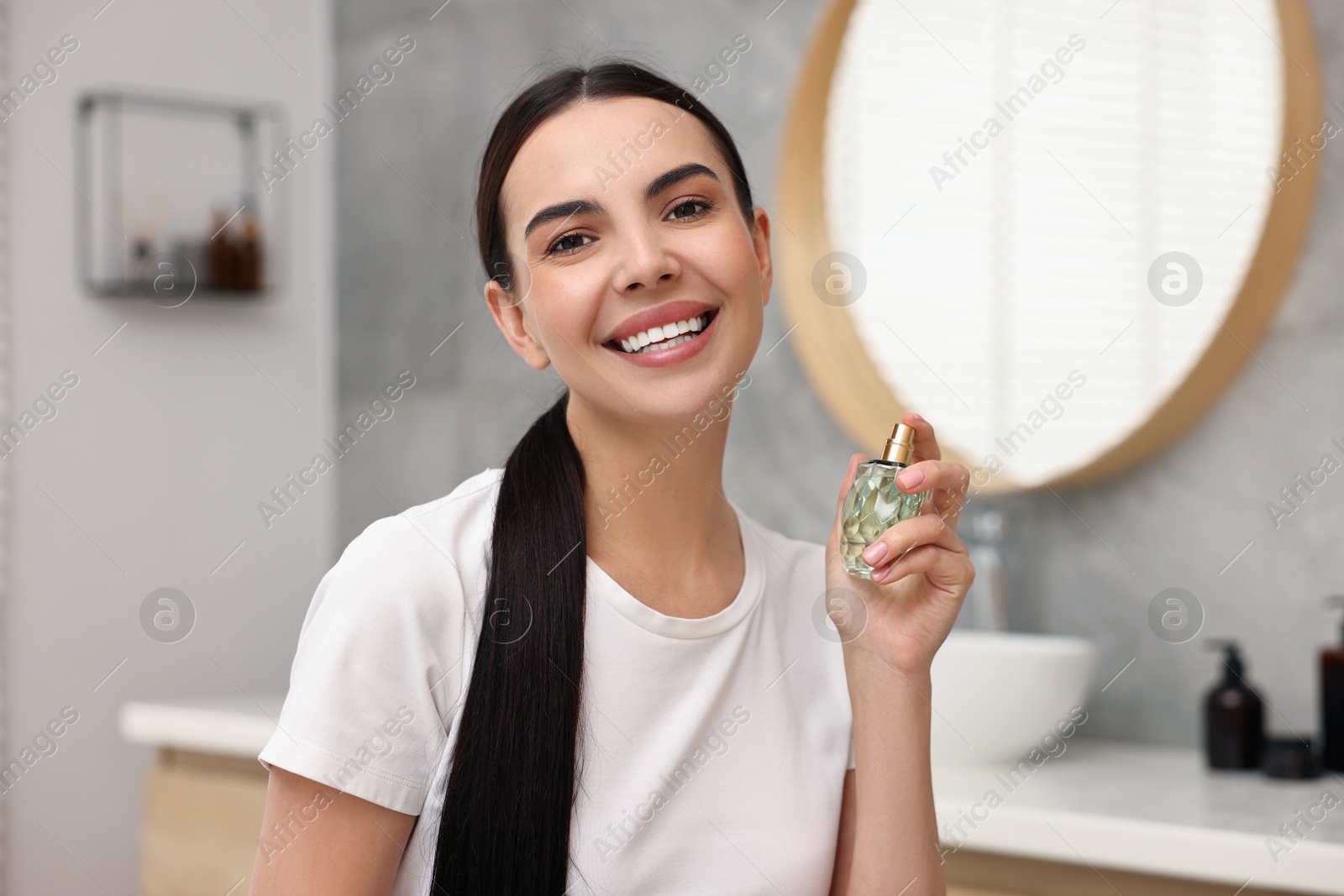 Photo of Smiling woman with bottle of perfume in bathroom