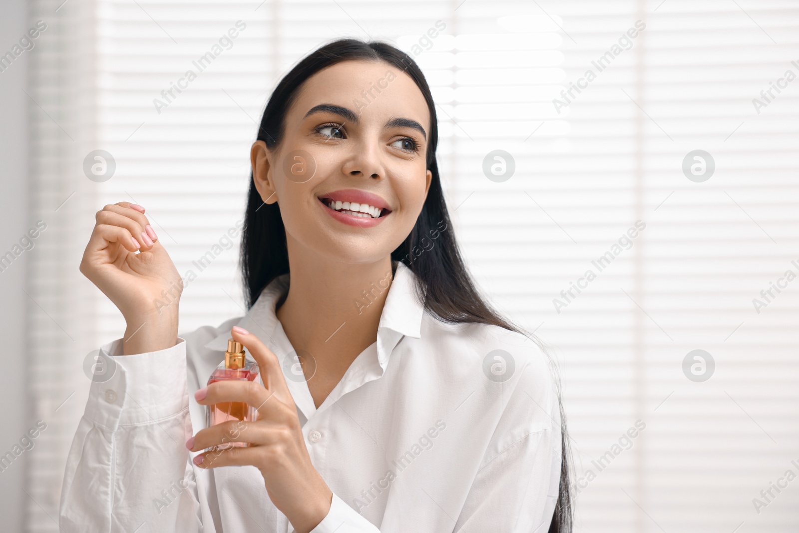 Photo of Smiling woman spraying aromatic perfume onto wrist at home. Space for text