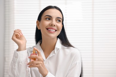 Smiling woman spraying aromatic perfume onto wrist at home. Space for text