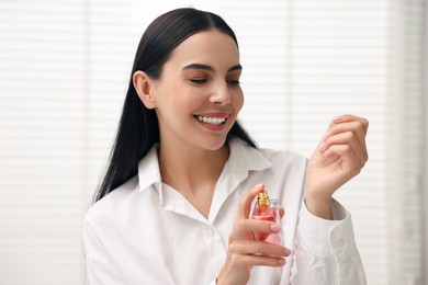 Smiling woman spraying aromatic perfume onto wrist at home