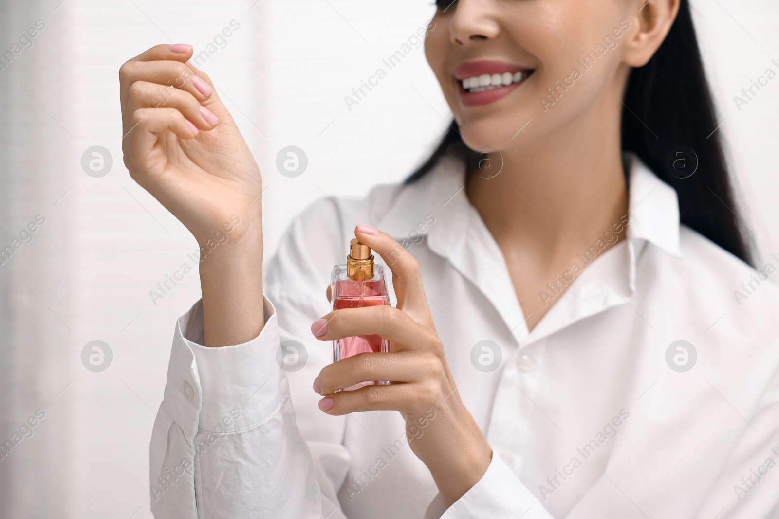 Photo of Smiling woman spraying perfume onto wrist at home, closeup