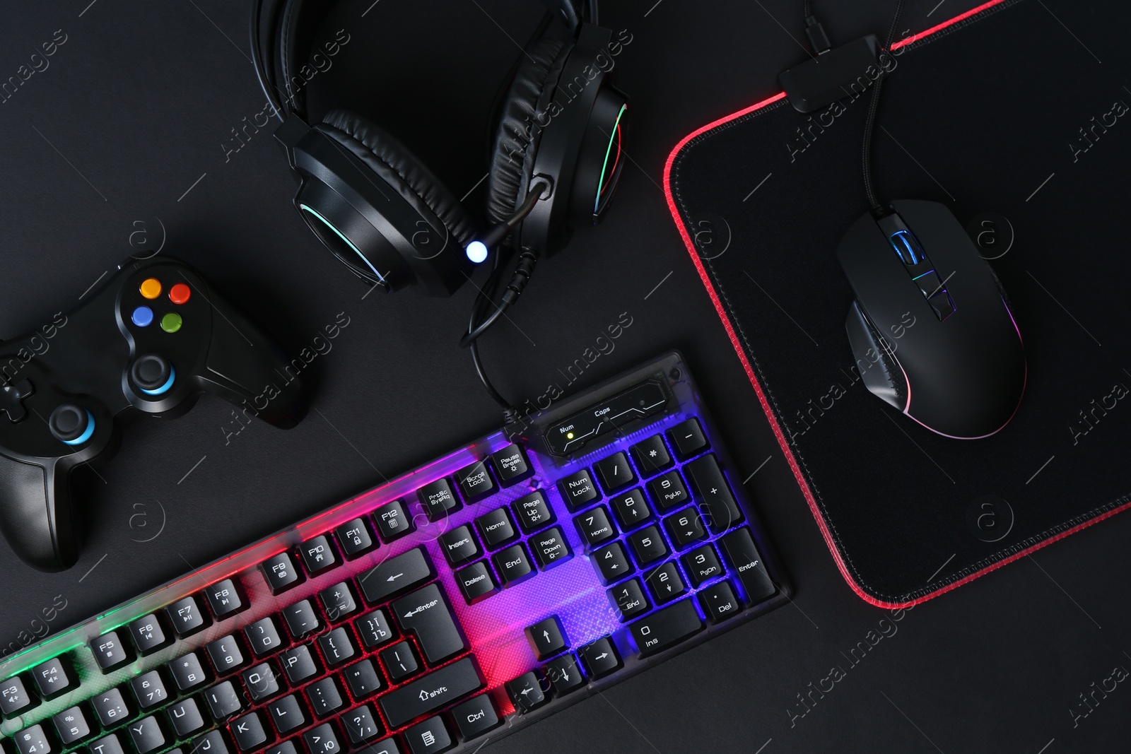 Photo of Computer mouse, RGB keyboard, game controller and headset on black background, flat lay