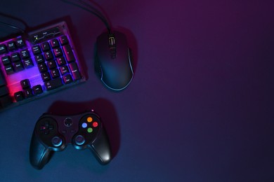 Computer mouse, RGB keyboard and game controller in neon lights on dark background, flat lay. Space for text