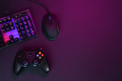 Computer mouse, RGB keyboard and game controller in neon lights on dark background, flat lay. Space for text