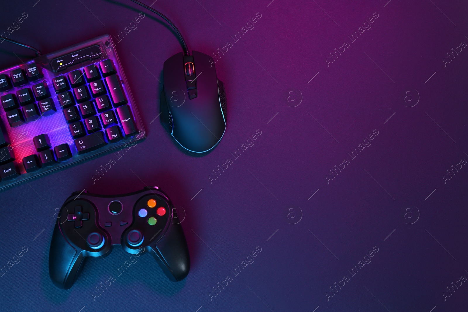 Photo of Computer mouse, RGB keyboard and game controller in neon lights on dark background, flat lay. Space for text