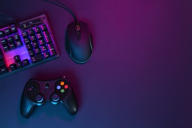 Photo of Computer mouse, RGB keyboard and game controller in neon lights on dark background, flat lay. Space for text