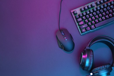 Computer mouse, RGB keyboard and headset in neon lights on dark background, flat lay. Space for text