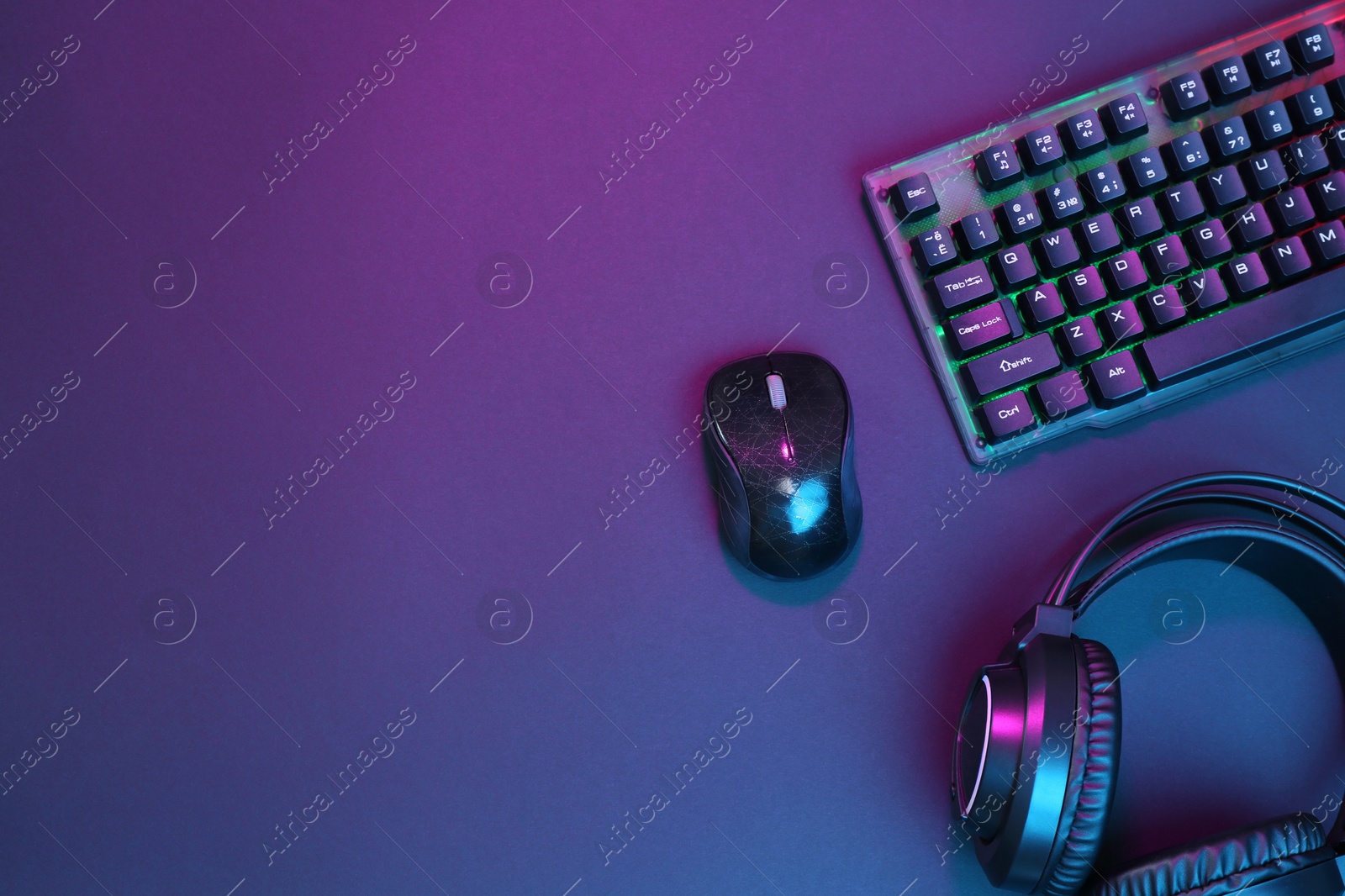 Photo of Computer mouse, RGB keyboard and headset in neon lights on dark background, flat lay. Space for text