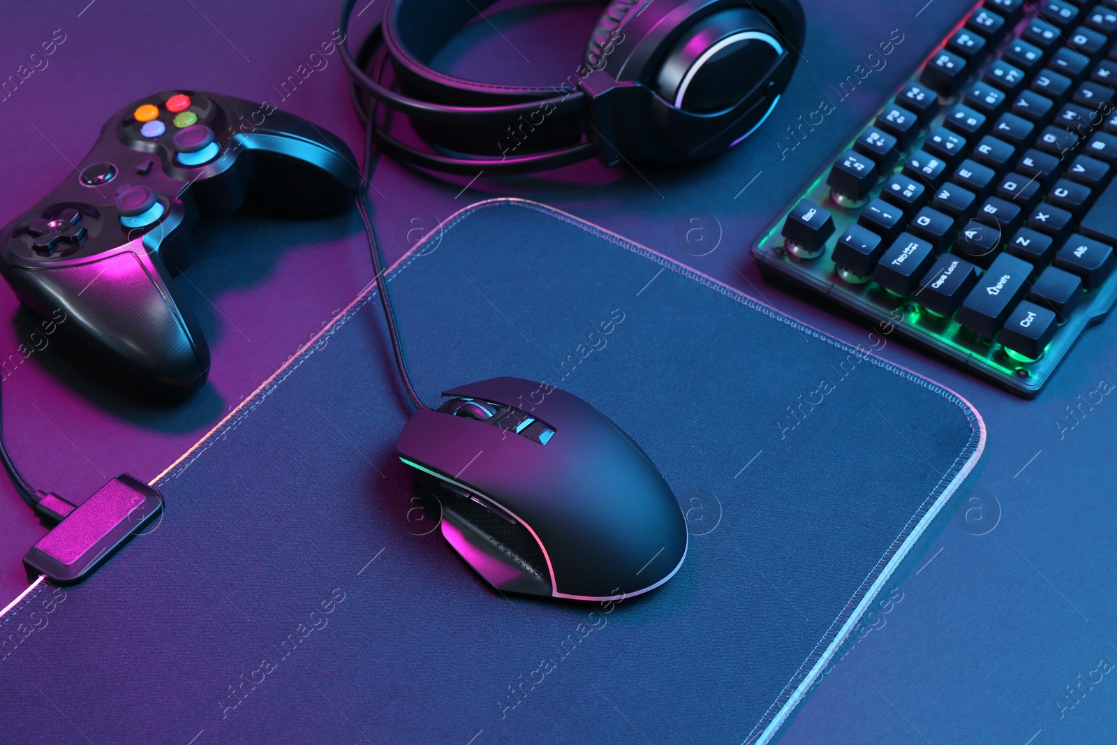 Photo of Computer mouse, RGB keyboard, game controller and headset in neon lights on dark background