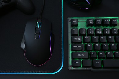 Computer mouse, RGB keyboard and game controller on black background, top view