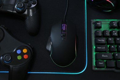 Photo of Computer mouse, RGB keyboard and game controllers on black background, top view