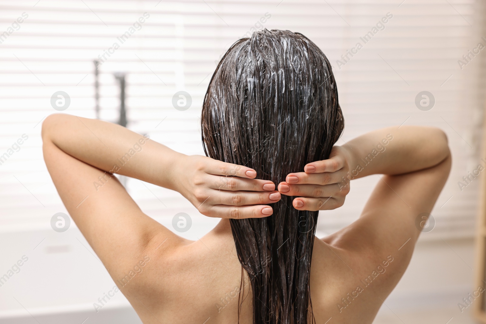 Photo of Woman applying hair mask in bathroom, back view