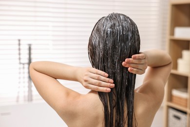 Photo of Woman applying hair mask in bathroom, back view