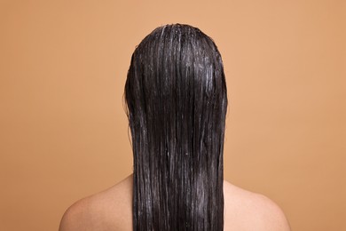 Woman with applied hair mask on beige background, back view