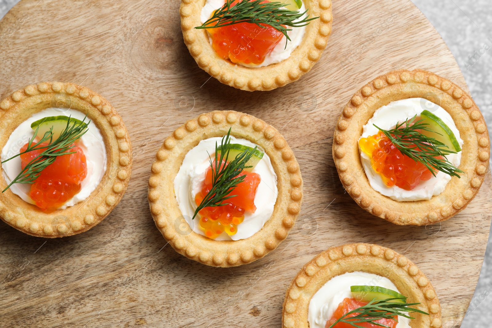 Photo of Delicious canapes with salmon and red caviar on wooden board, top view