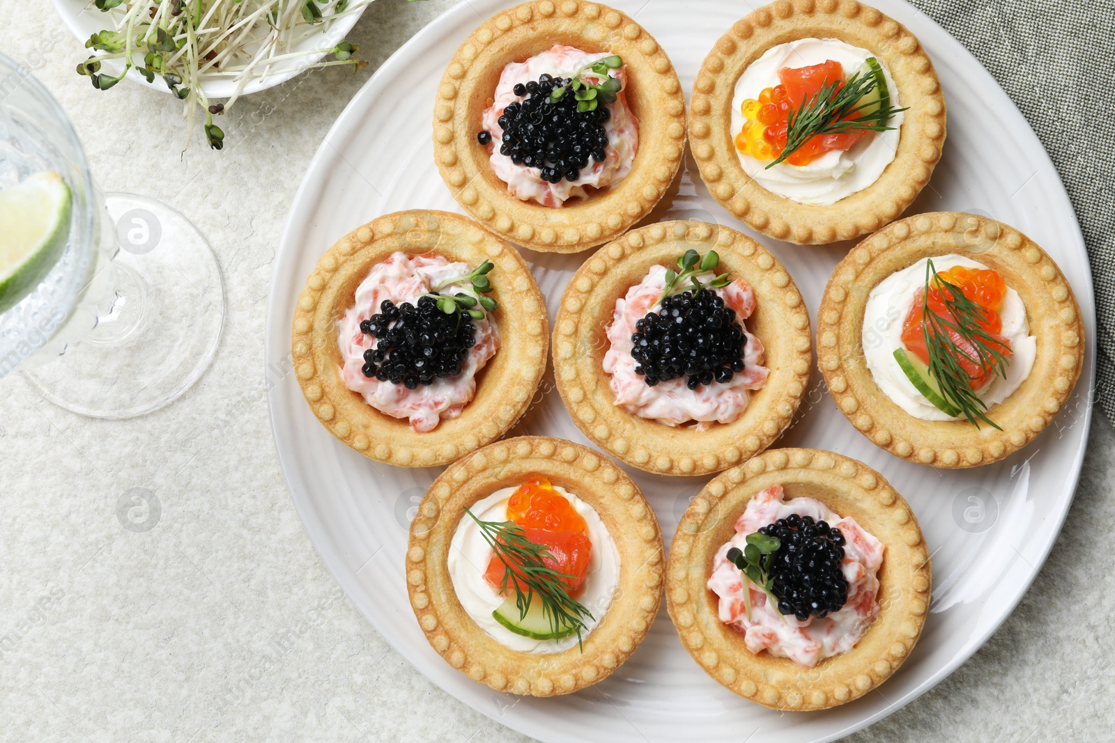 Photo of Delicious canapes with salmon, caviar, microgreens and glass of water on beige textured table, flat lay