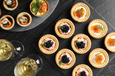 Photo of Delicious canapes and glasses of white wine on black textured table, flat lay