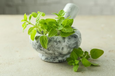 Photo of Fresh green oregano in mortar and pestle on light textured table, closeup