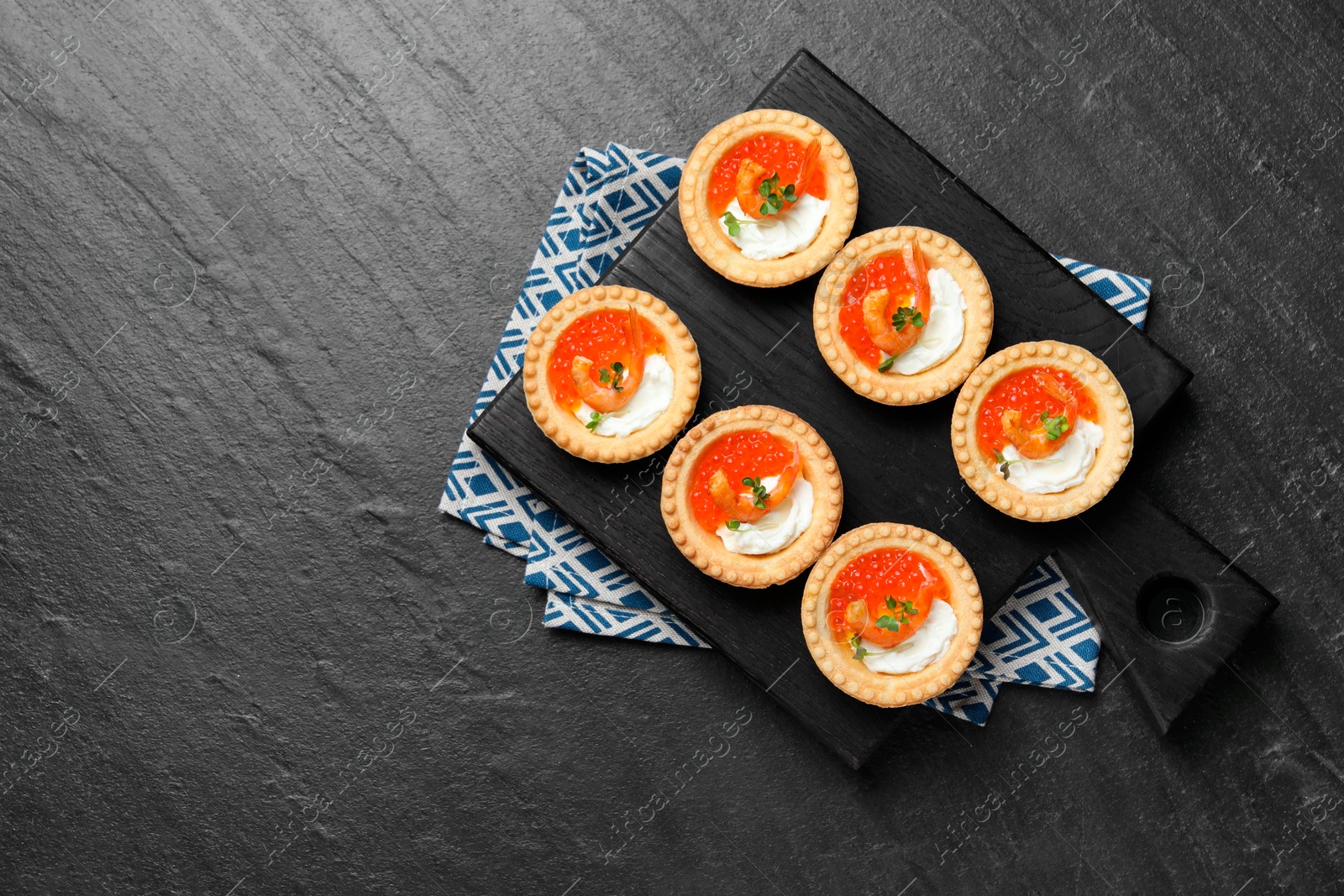 Photo of Delicious canapes with shrimps, red caviar and cream cheese on dark textured table, top view. Space for text