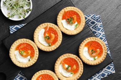 Delicious canapes with shrimps, red caviar and cream cheese on dark textured table, flat lay