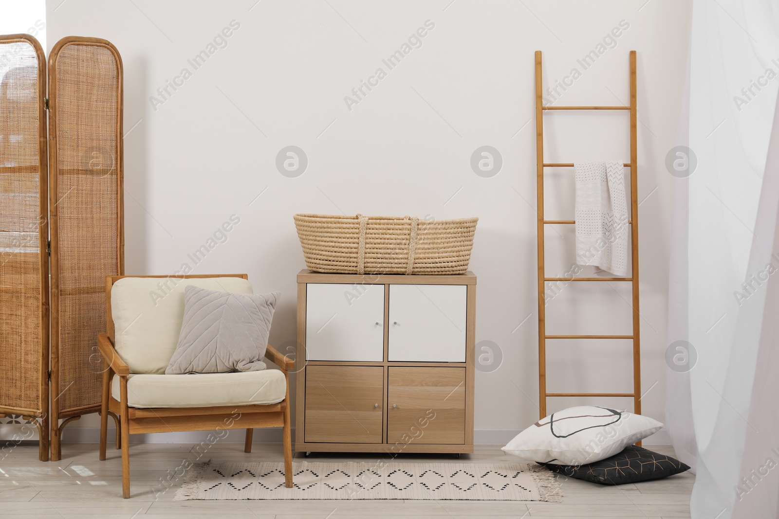 Photo of Armchair with cushion, wicker basket on nightstand and wooden ladder in room