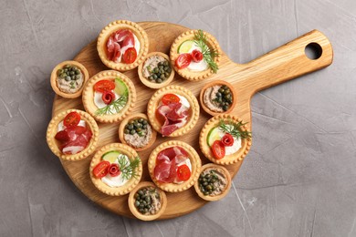 Photo of Delicious canapes with jamon, pate and dry smoked sausages on grey textured table, top view