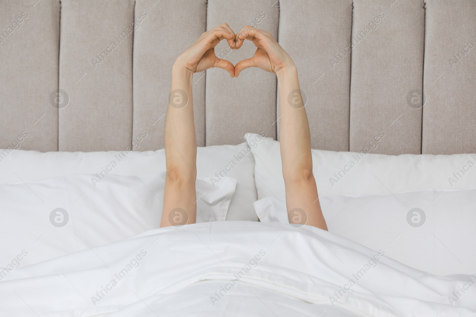 Photo of Good morning. Woman making heart gesture with hands in bed, closeup