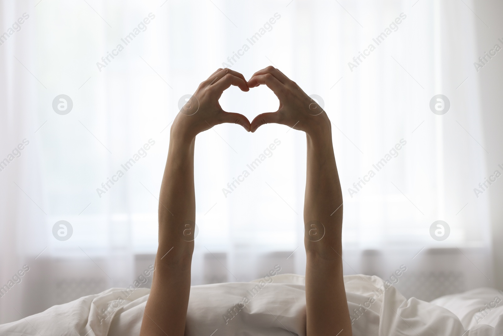 Photo of Good morning. Woman making heart gesture with hands at home, closeup