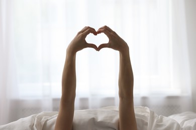 Good morning. Woman making heart gesture with hands at home, closeup