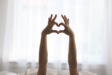 Photo of Good morning. Woman making heart gesture with hands at home, closeup