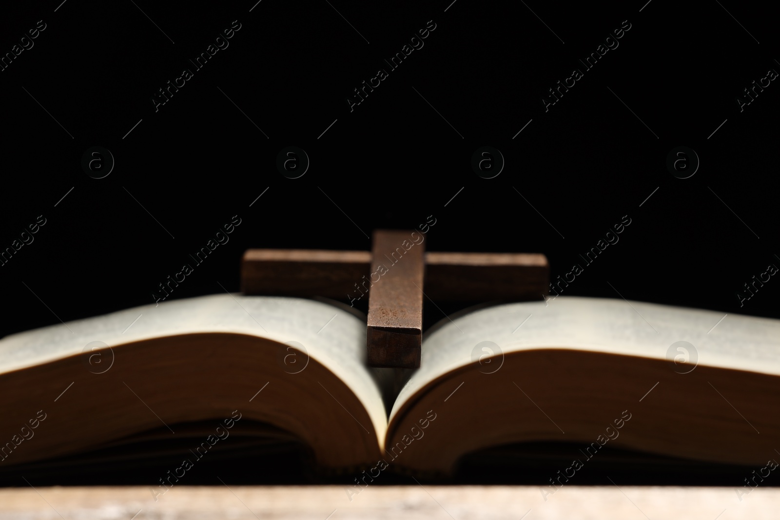 Photo of Bible and cross on table against black background, closeup with space for text. Religion of Christianity