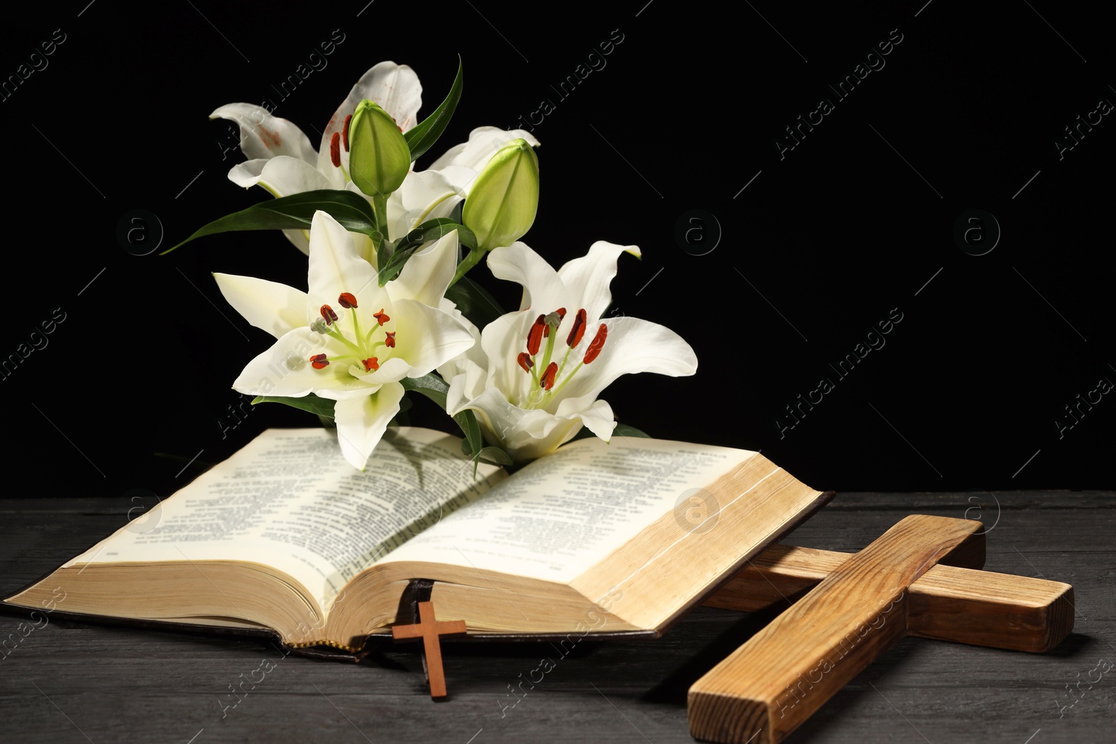 Photo of Bible, crosses and lilies on dark gray wooden table against black background. Religion of Christianity