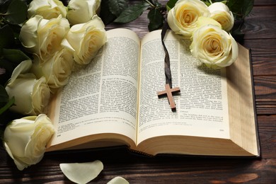 Photo of Bible, cross and roses on wooden table, closeup. Religion of Christianity