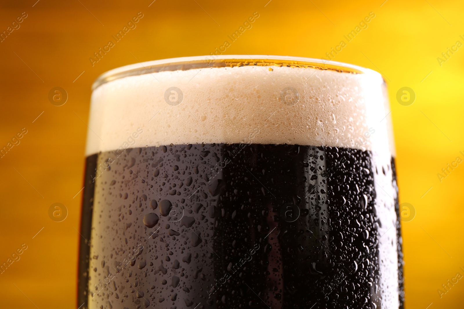 Photo of Glass of beer with froth on yellow background, closeup